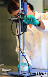 Person in lab coat and green plastic glove handling lab-equipment. Photo.