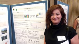 Woman standing next to posterboard, looking into the camera. Photo.