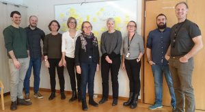 Nine people posing for photo in front of whiteboard. Photo.