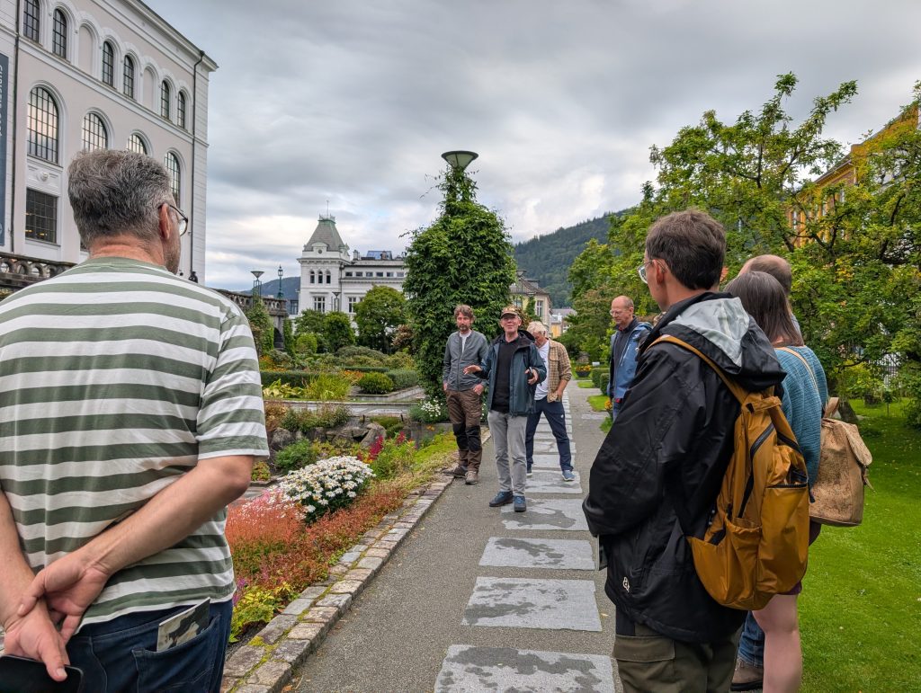 People in a garden with beautiful plants and white stone buildings.
