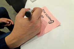 Close up on hand writing on a pink post-it. Photo.