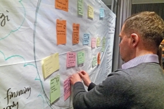 Man looking at a white board with post-it notes on it. Photo.
