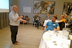 Man standing infront of a table gesturing. Photo.