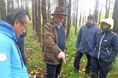 Group of people outside in forest looking at the ground. Photo.