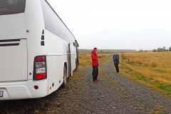 White buss and two people standing next to it. Photo.