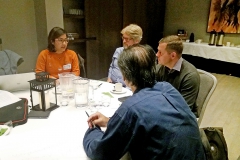 Four people sitting at a white table, talking. Photo.
